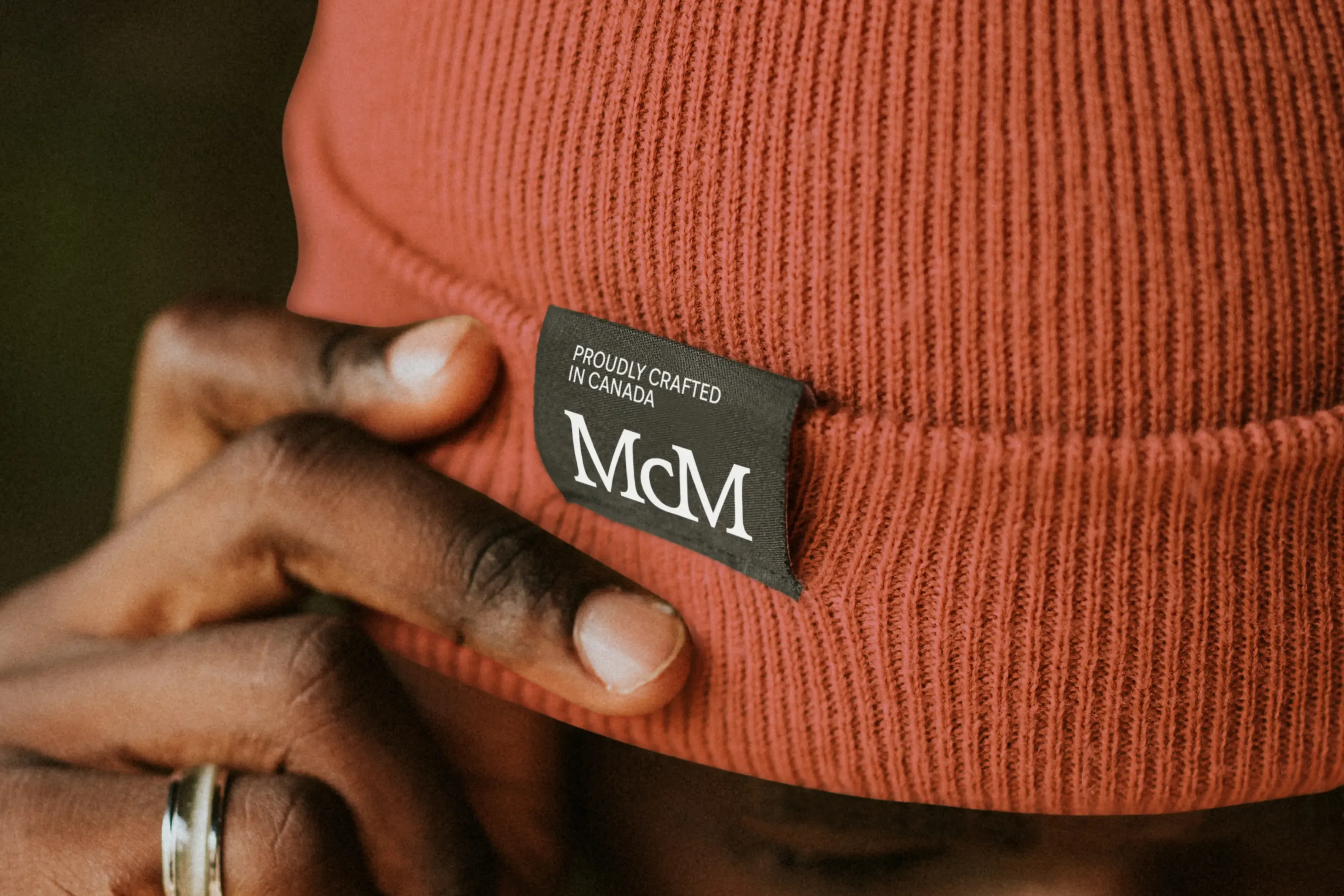 Closeup of a tag on a rust coloured beanie that is embroidered with the McMichael monogram and words that say